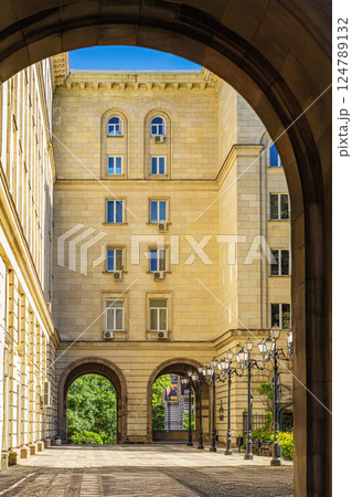 Stone archway frames sunlit facade of building with neoclassical windows. Stone structure symbolizes authority, tradition, classic style Stone archway frames sunlit facade of building with neoclassical windows. Stone structure symbolizes authority, tradition, classic style 124789132