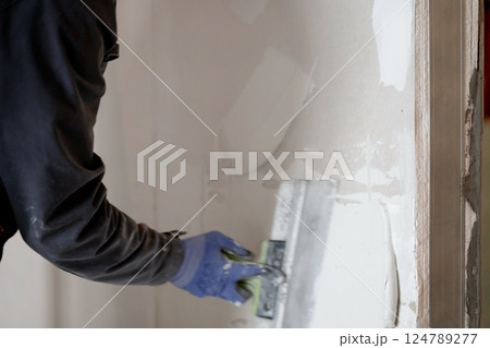 The worker's hands putty the wall with a spatula. Apartment renovation. Sealing openings between drywall. With space to copy. High quality photo 124789277