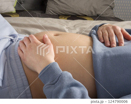 Pregnant woman resting peacefully, gently touching round belly, reflecting intimate maternal bonding and emotional anticipation of incoming newborn 124790006