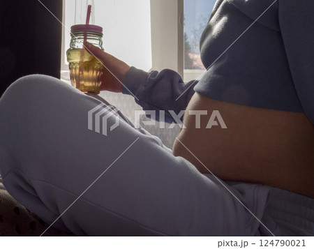 Pregnant woman relaxing indoors, sipping fresh juice, embodying wellness and nurturing her growing baby with mindful nutrition and calm 124790021