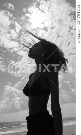 Woman enjoying a breezy moment by the beach under a partly cloudy sky 124791213