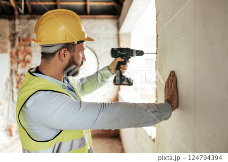 Construction worker, man or drilling wall with electric tool for utility lines, pipes or duct work in office building property. Engineering worker or architect drill on real estate construction site 124794394