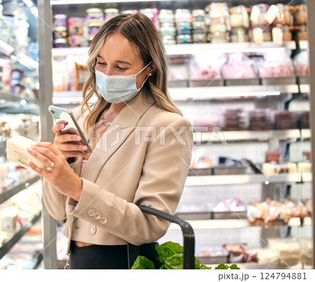 Grocery store, woman covid mask and phone food ingredient check of a retail customer. Groceries shop of a person looking at a mobile app for a healthy diet label shopping in a supermarket checking 124794881