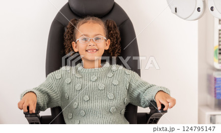 Girl child, eye test glasses and smile in portrait at optometrist office, clinic or hospital for visual impairment. Young, female kid sitting or examination of eyes, sight and vision at optical exam 124795147