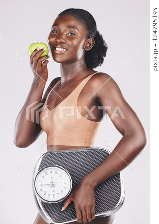 Apple, scale and weightloss with a black woman in studio on a gray background to promote healthy eating or diet. Food, fruit and exercise with an attractive young female posing for natural vitamins Apple, scale and weightloss with a black woman in studio on a gray background to promote healthy eating or diet. Food, fruit and exercise with an attractive young female posing for natural vitamins 124795195