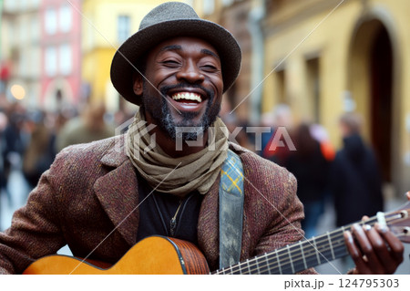 Man in a hat and scarf plays guitar, smiling broadly, standing in a lively street. Concept of music and happiness. For stock photo on joy and music culture. Man in a hat and scarf plays guitar, smiling broadly, standing in a lively street. Concept of music and happiness. For stock photo on joy and music culture. 124795303