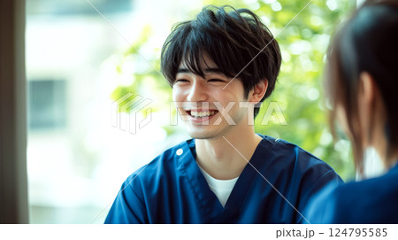 Smiling person in blue scrubs in a bright, soft-focus environment with greenery in the background. Concept of healthcare professional, happiness, positivity. For medical services photos. Smiling person in blue scrubs in a bright, soft-focus environment with greenery in the background. Concept of healthcare professional, happiness, positivity. For medical services photos. 124795585