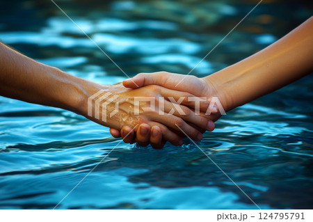 Two hands grasp each other above a calm blue water surface, creating a sense of connection. Concept of unity and togetherness. For relationship and support themes. Two hands grasp each other above a calm blue water surface, creating a sense of connection. Concept of unity and togetherness. For relationship and support themes. 124795791