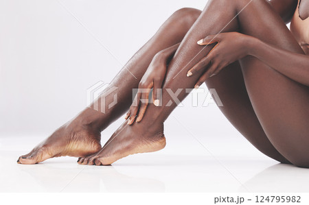 Feet, legs and skincare with a model black woman touching her soft or smooth skin in studio on a gray background. Hands, skin and luxury with a female rubbing her foot or ankle for beauty or wellness 124795982