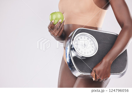 Fitness, wellness and black woman with scale and apple in hand, isolated on white background in studio. Exercise, nutrition and slim woman on diet for healthy lifestyle, weight loss and body care 124796056
