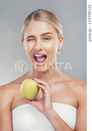 Woman, health and wink portrait with apple for fiber diet, nutrition and wellness lifestyle. Fruit, healthy and digestion dieting marketing with happy model girl on gray studio background. Woman, health and wink portrait with apple for fiber diet, nutrition and wellness lifestyle. Fruit, healthy and digestion dieting marketing with happy model girl on gray studio background. 124796126