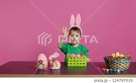 Excited little kid decorating baskets with eggs and grass to prepare for easter holiday festivity, creating festive arrangements. Cute toddler with bunny ears does craft activity. Camera B. 124797019