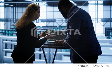 Team of developers doing maintenance checkup using laptop to prolong data center hardware life span. IT support staff members in server hub monitor server infrastructure using notebook, camera A 124797020
