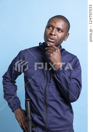 Pensive african american agent contemplating about his responsibility, working on safeguarding a property. Male security guard acting thoughtful, patrol duty in front of camera. Pensive african american agent contemplating about his responsibility, working on safeguarding a property. Male security guard acting thoughtful, patrol duty in front of camera. 124797033