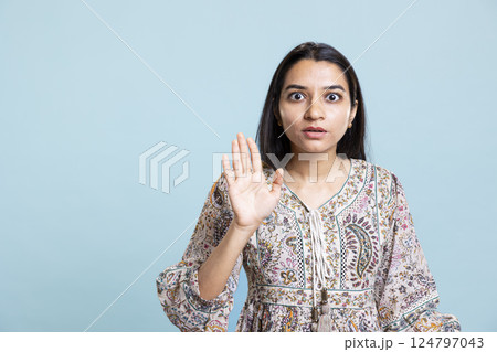 Stern indian woman doing stop hand gesture sign and complaining in studio. Authoritative person doing firm rejection symbol with her palm, having enough against blue background. Stern indian woman doing stop hand gesture sign and complaining in studio. Authoritative person doing firm rejection symbol with her palm, having enough against blue background. 124797043