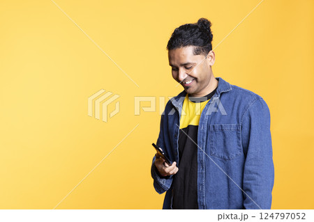 Indian adult chatting with people on remote telephone line in studio, discussing with his friends or close ones against orange background. Young confident joyous man with man bun on a phone call. 124797052