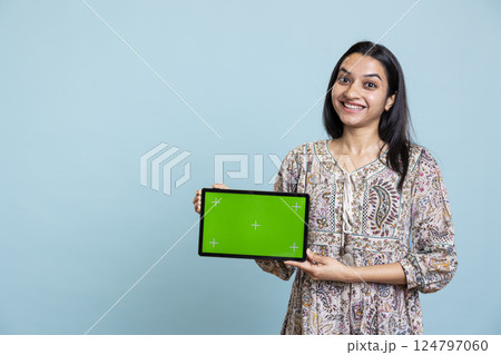 Indian girl smiling and showing isolated copy space screen in front of camera, creating an advertisement for a commercial against blue background. Young joyful adult holding device in studio. 124797060