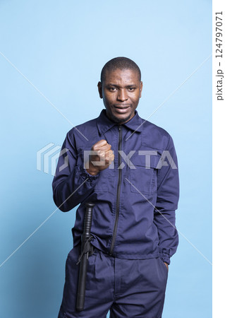 Happy security guard cheering about something in studio, feeling very pleased and enthusiastic in front of camera. Confident bodyguard in uniform with baton showing positivity while on duty. Happy security guard cheering about something in studio, feeling very pleased and enthusiastic in front of camera. Confident bodyguard in uniform with baton showing positivity while on duty. 124797071