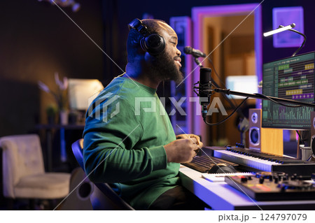Young producer performing a live acoustic song in home studio, recording a new track on microphone and using DAW software. Artist songwriter editing the audio files in post production. Young producer performing a live acoustic song in home studio, recording a new track on microphone and using DAW software. Artist songwriter editing the audio files in post production. 124797079