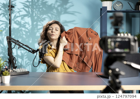 Content creator filming sponsored fashion vlog, unboxing jacket from internet order, mimicking surprise to get subscribers to make purchases from sponsor, doing influencer marketing 124797094