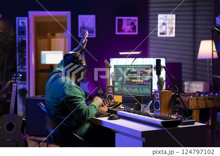 Confident music composer mixing sounds on digital audio software, creating a cool atmosphere in his home studio. Young cheerful producer composing new soundtracks with stereo gear. 124797102