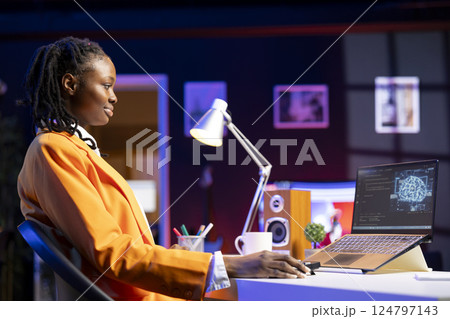 Smiling woman using laptop in apartment, updating artificial intelligence machine learning algorithms, writing code. Upbeat teleworking IT expert working from home uses programming to upgrade AI 124797143