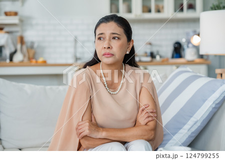 Upset Asian senior woman sitting on sofa, lost in thoughts, feeling lonely Upset Asian senior woman sitting on sofa, lost in thoughts, feeling lonely 124799255