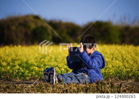 ＜花と人物＞菜の花をスマホで撮影する少年 124800263