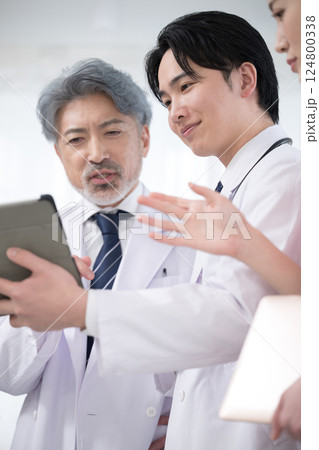 カルテや診察などの状況を確認するチーム医療の医師たち、 指導医と研修医のイメージ 124800338