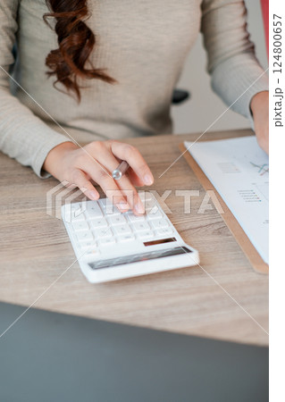 Close-up of a woman calculating finances with a calculator and documents on a wooden desk, highlighting business and finance concepts. 124800657