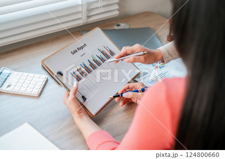 Professional woman reviewing sales data on a clipboard, highlighting business growth and analysis in a contemporary office environment. 124800660
