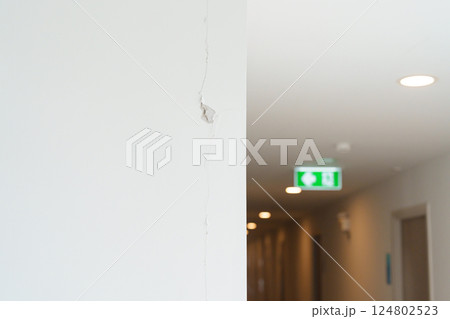 Cracked concrete wall broken wall after Earthquake effect. Damage building with Emergency Exit door sign for emergency. Stairwell fire for escape in building or apartment Cracked concrete wall broken wall after Earthquake effect. Damage building with Emergency Exit door sign for emergency. Stairwell fire for escape in building or apartment 124802523