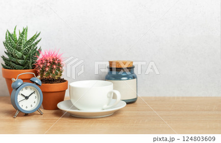 Coffee cup, alarm clock and cacti creating relaxing morning atmosphere on desk Coffee cup, alarm clock and cacti creating relaxing morning atmosphere on desk 124803609