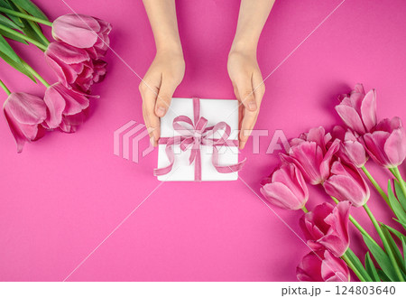 Gift box in hands with flowers tulips on pink background. happy mothers day, top view. copy space Gift box in hands with flowers tulips on pink background. happy mothers day, top view. copy space 124803640