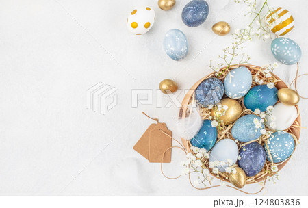 Easter eggs in the nest. Easter background with colorful eggs in a basket on a white wooden background. top view. copy space 124803836