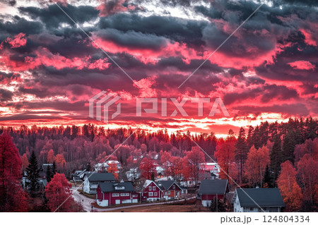 A vibrant sunset casts deep reds and oranges across the sky, reflecting over a small rural town surrounded by fiery autumn foliage. The scene captures serene beauty at dusk. A vibrant sunset casts deep reds and oranges across the sky, reflecting over a small rural town surrounded by fiery autumn foliage. The scene captures serene beauty at dusk. 124804334
