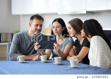 Interracial group of friends checking tablet in a kitchen Interracial group of friends checking tablet in a kitchen 124805881
