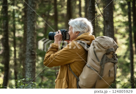 A middle aged woman with white hair is taking photos in the forest. 124805929