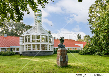 A contemporary building with large glass windows and a clock tower, set in a lush green landscape with trees and clear skies. 124806652