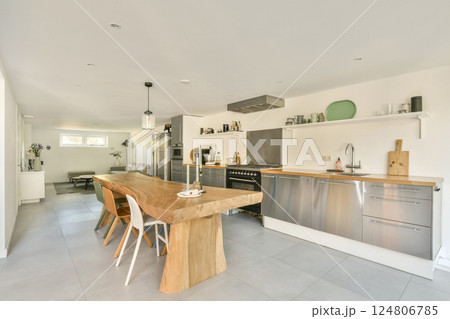 A spacious and contemporary kitchen featuring a wooden dining table, stainless steel appliances, and a sleek design, perfect for modern living. 124806785