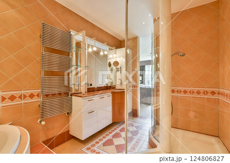 A stylish modern bathroom showcasing elegant design with tiled walls, glass shower, and sleek cabinetry. Bright and inviting ambiance for relaxation. 124806827