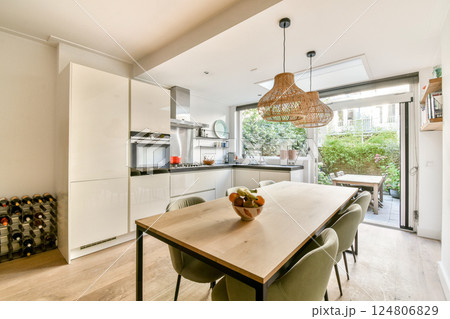 Stylish kitchen interior featuring white cabinetry, a wooden dining table, and ample natural light from windows, creating a bright, inviting atmosphere. Stylish kitchen interior featuring white cabinetry, a wooden dining table, and ample natural light from windows, creating a bright, inviting atmosphere. 124806829