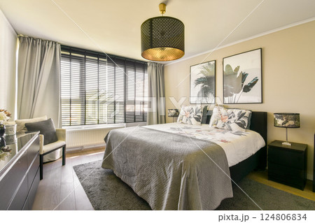 A beautifully designed modern bedroom featuring a comfortable bed, elegant decor, and ample natural light streaming through large windows. 124806834