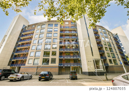 A contemporary residential building showcasing modern architectural design, featuring multiple balconies and large windows against a clear blue sky. 124807035