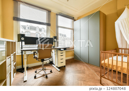 A stylish home office combined with a cozy nursery, featuring a sleek desk, comfortable chair, and modern storage solutions in warm colors. A stylish home office combined with a cozy nursery, featuring a sleek desk, comfortable chair, and modern storage solutions in warm colors. 124807048