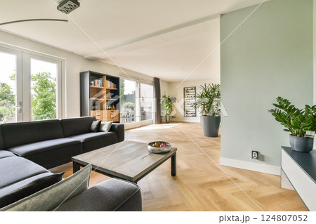 A contemporary living room featuring a cozy couch, wooden flooring, and greenery, creating an inviting and stylish atmosphere for relaxation. 124807052
