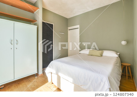 A serene modern bedroom featuring a neatly made bed, light green walls, minimal furniture, and a calming atmosphere ideal for relaxation. 124807340