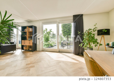 A contemporary living room featuring large windows, stylish furniture, and vibrant indoor plants, creating a bright and welcoming atmosphere. 124807353