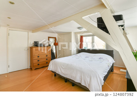 This serene bedroom features a comfortable bed, wooden furniture, and ample natural light, creating a peaceful living space for relaxation. 124807392