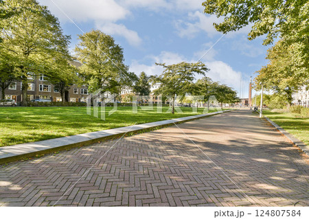 A serene pathway winding through a lush city park, framed by vibrant trees and modern buildings, inviting visitors to enjoy nature and relaxation. 124807584